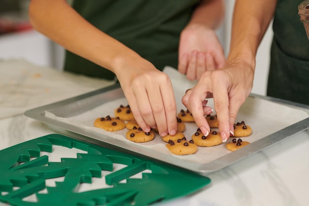 Hände von Mutter und Tochter dekorieren Kekse mit Schokoladenstückchen