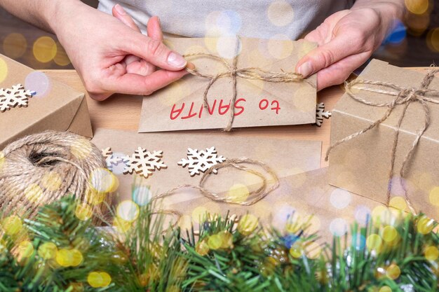 Hände wickeln einen Weihnachtsbrief in einen Umschlag mit den Worten TO SANTA auf einem Tisch mit Christm