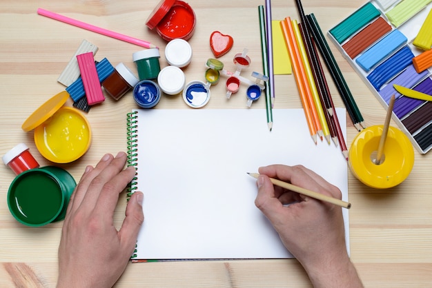 Hände zeichnen mit Farben und Markierungen auf weißem Papier