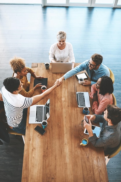 Händeschütteln oben und Geschäftsleute in einem Meeting am Arbeitsplatz zum Onboarding und zur Begrüßung. Fröhliches Vorstellungsgespräch und Unternehmensmitarbeiter, die sich in einer Gruppendiskussion die Hand für ein Dankeschön oder eine Partnerschaft schütteln