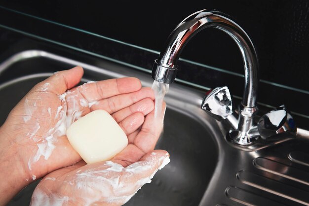 Händewaschen mit Seife unter fließendem Wasser. Stück Seife auf den Handflächen von Männern unter Wasserstrahl vor dem Hintergrund einer Metallspüle.