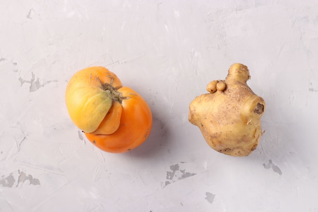 Foto hässliche tomate und kartoffel auf hellgrauem hintergrund, nahaufnahme, hässliches essen consept, draufsicht