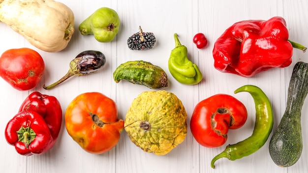Hässliches Bio-Gemüse Gurke, Paprika, Aubergine, Brombeere, Hartriegel, Kürbis, Zucchini, Birne und Tomaten auf weißem Tisch, hässliches Lebensmittelkonzept, Draufsicht