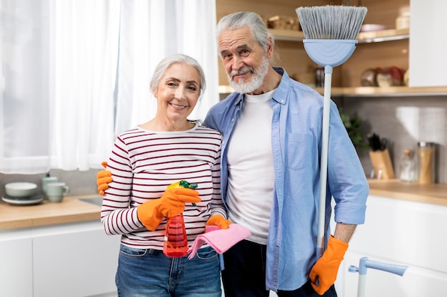 Häusliche Aufgaben Konzept Glückliche ältere Ehepartner posieren mit Reinigungsmitteln in der Küche