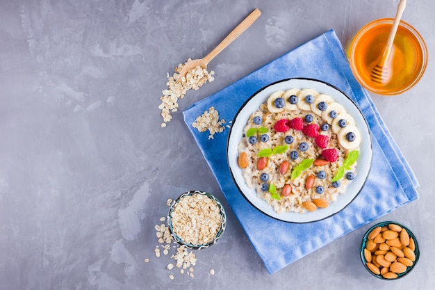 Haferbrei mit Beeren, Früchten und Honig auf grauem Hintergrund