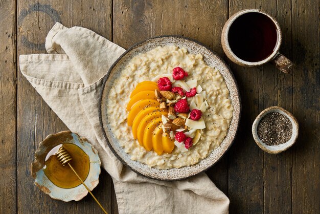 Haferbrei mit Pfirsich Himbeeren Mandeln Nüssen Kokoschips Chiasamen Honig und Tee