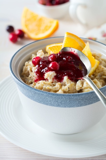 Haferbrei mit Preiselbeersauce und Orange in einer Keramikschale auf einer hellen Oberfläche. Selektiver Fokus.