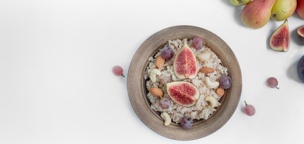 Haferflocken in einem Teller mit frischen Feigen, Mandeln, Cashewnüssen und frischen Früchten auf weißem Grund. Haferflocken mit Früchten. Gesundes Frühstück. Banner mit Essen. Speicherplatz kopieren.