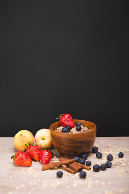 Haferflocken mit Blaubeeren und Erdbeeren in einem Holzteller. Pfirsiche und Beeren auf dem Tisch.