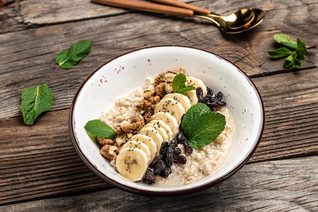 Haferflocken mit getrockneten Rosinen Banane und Walnüssen mit Minze dekoriert Gesunde Ernährung vegetarisches Frühstück oder Snack Clean Eating diätendes veganes Lebensmittelkonzept Draufsicht