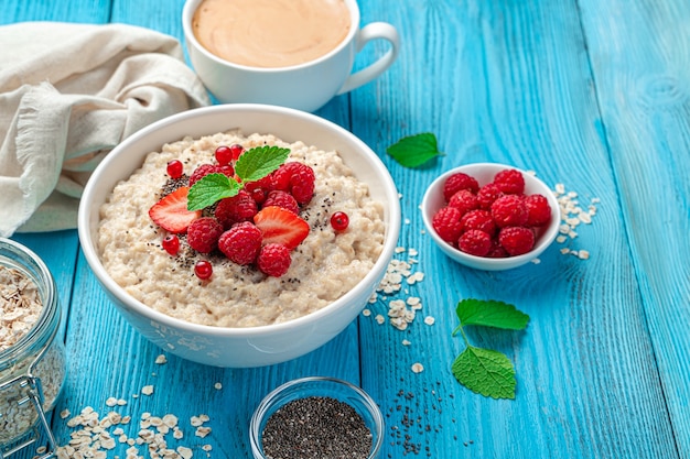 Haferflocken mit Himbeeren, Erdbeeren und roten Johannisbeeren in einem weißen Teller auf blauem Hintergrund