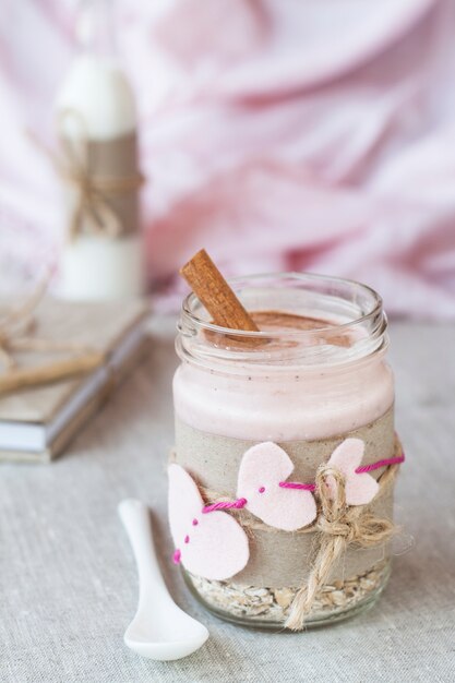 Haferflocken, mit Joghurt gewürzt, mit Zimt in einem Glas bestreut. Als nächstes kommt eine Flasche Milch. Als nächstes kommt ein Bastelheft und eine rosa Serviette.