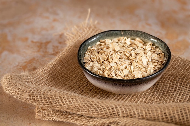 Haferflocken Müsli in einer handgefertigten Keramikschale auf Sackleinen auf einem beigen Steintisch kopieren