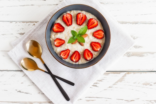 Haferflocken-Porridge mit Erdbeeren in dunkler Schüssel. Gesundes Frühstück mit Haferflocken und frischen Bio-Beeren, Draufsicht, Kopierraum.