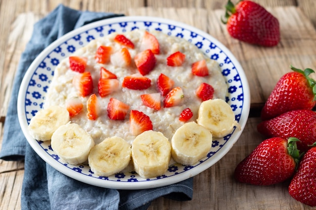 Haferflocken-Porridge mit Erdbeeren und Banane auf rustikalem Holztisch