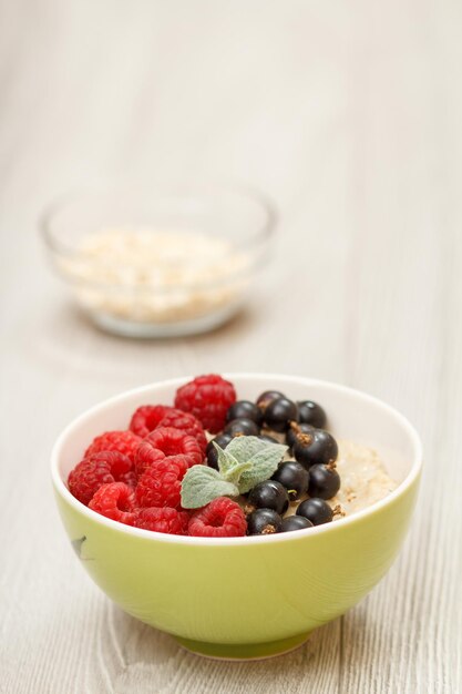 Haferflockenbrei in porzellanschale mit johannisbeeren und himbeeren dekoriert mit minzblättern