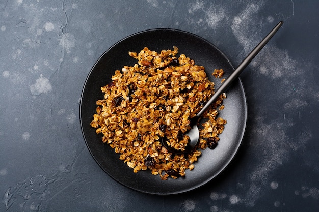 Haferflockenmüsli mit getrockneten Früchten, Chiasamen und Sonnenblumen, Honig in schwarzer Keramikplatte. Draufsicht.