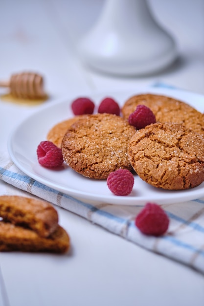 Haferflockenplätzchen mit Honig verziert mit Himbeeren. Dessert auf einem Handtuch auf einem weißen Küchentisch Nahaufnahme.