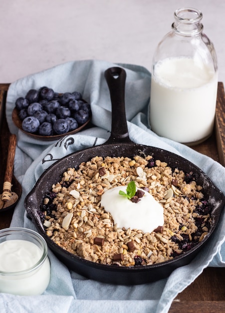 Haferflockenstreusel in Gusseisenpfanne mit frischen Heidelbeeren und Naturjoghurt.