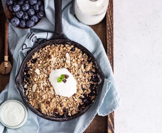 Haferflockenstreusel in Gusseisenpfanne mit frischen Heidelbeeren und Naturjoghurt.