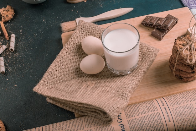 Haferkekse mit Schokoladenstückchen, Eiern und einem Glas Milch auf einem Holzbrett