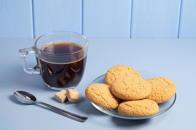 Haferkekse und eine Tasse heißen Kaffee in transparenten Schalen auf blauem Tisch