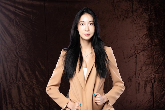 Haft body portrait der schönen transgender-asiatin der 20er jahre drückt das gefühl aus, selbstbewusst auf braunem hintergrund zu lächeln business female smart look blazer hat windschlag, der ihr haar in den luftkopierraum wirft