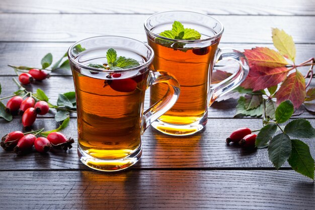Hagebutten-Tee in transparenter Tasse mit Honig und frischen Beeren. Vitamin C Getränk auf dunklem Tisch