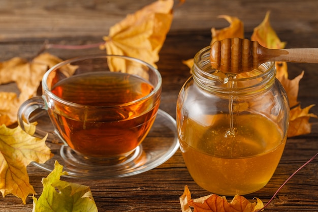 Hagebutten-Tee in transparenter Tasse und Teekanne mit Honig und Herbstlaub. heißes Herbstgetränk