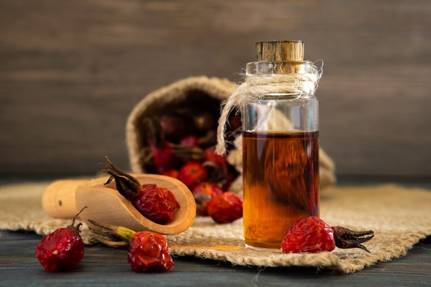 Hagebuttenöl auf Holzbrettern auf dunklem Hintergrund. Die Flasche ist mit einer Schnur mit ätherischem Heckenrosenöl gebunden. Tüte Beeren.