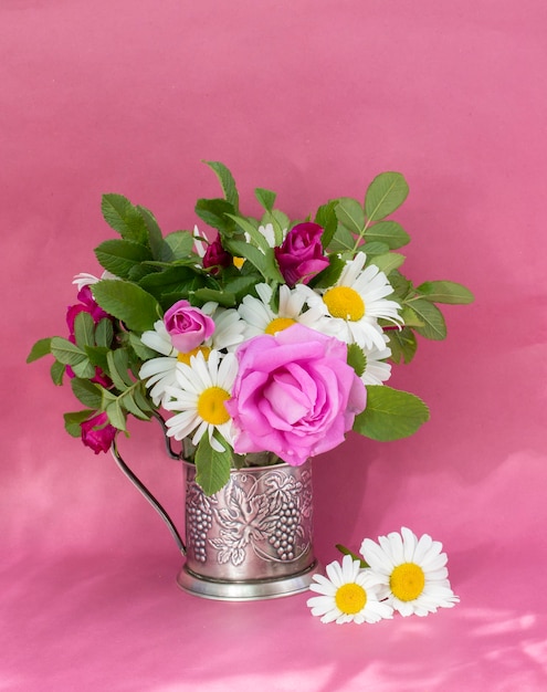 Hagebuttenrose und Kamille Bouquet. Sommerstrauß von Gartenblumen. Stillleben auf dem rosa Hintergrund