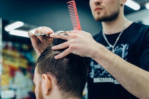 Hairstylist masculino que corta o cabelo de um cliente