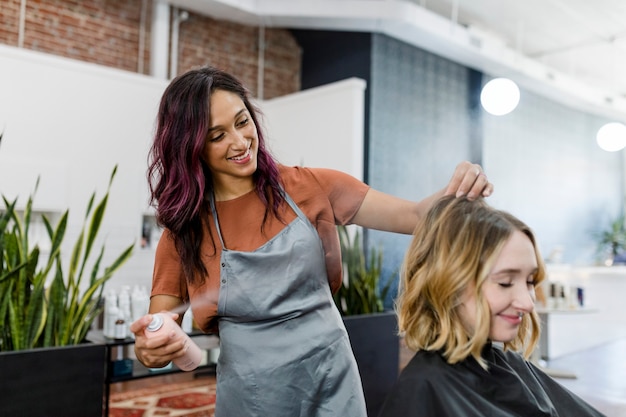 Hairstylistin sprüht ihrer Kundin eine Maus auf die Haare