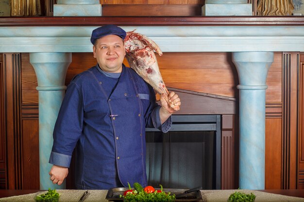 Halber Beinschuß des durchdachten männlichen Chefs, hält sehr großes rotes rohes Stück Fleisch.