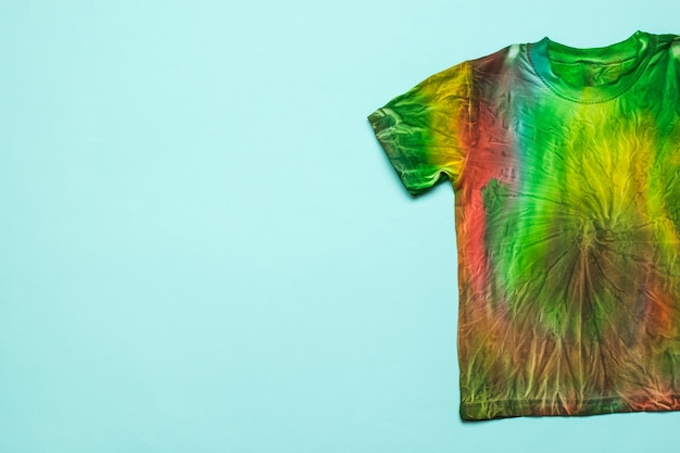 Halbes T-Shirt im Tie-Dye-Stil auf hellblauem Grund. Platz für den Text. Kleidung zu Hause von Hand färben. Flach liegen.