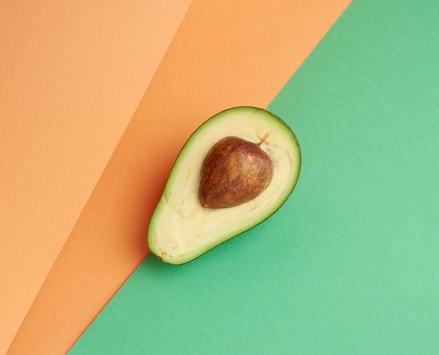 Halbreife grüne Avocado mit einem braunen Knochen auf einem abstrakten grün-orange Hintergrund