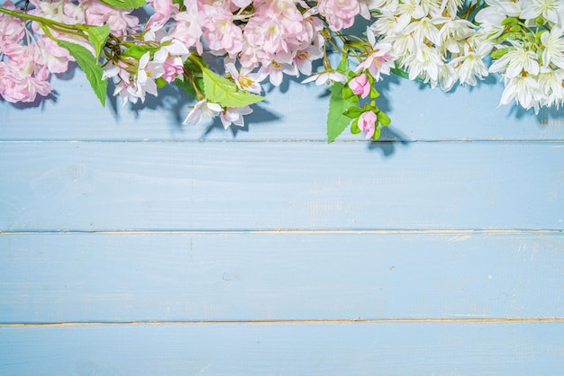 Hallo Frühlingskonzept Frühlingsferien Grußkarte einfacher Flatlay Hintergrund mit künstlichen Blüten Frühlingsblumen auf hellblauem Holzgartentisch Hintergrundrahmen Kopierraum Draufsicht