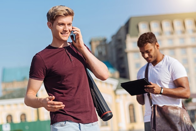 Hallo Mann. Junge männliche Person, die ein Lächeln auf seinem Gesicht hält und am Telefon spricht, während sie aktiv gestikuliert