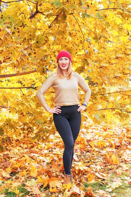 Hallo november. fröhliche stilvolle frau mit rotem hut unter herbstlaub draußen im stadtpark im herbst.