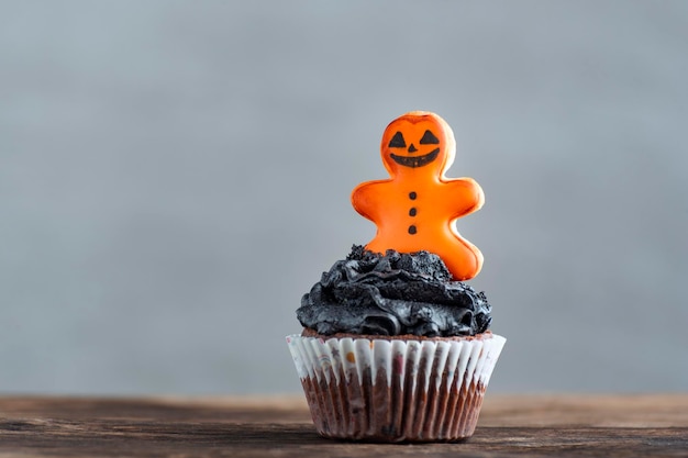 Halloween Cupcakes mit Lebkuchenmann auf Holztisch auf grauem Hintergrund Köstliche Halloween-Party-Muffins