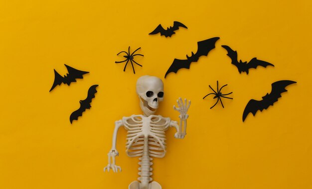 Halloween, decoraciones y concepto aterrador. Esqueleto y arañas, murciélagos negros vuelan sobre amarillo