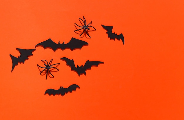 Halloween, decorações e conceito assustador. Aranhas e morcegos pretos voam sobre laranja brilhante