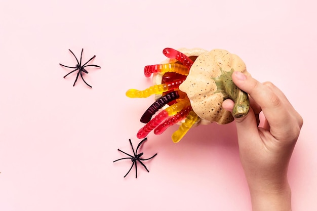 Halloween-Dekorationen Kinderhand öffnet Kürbis mit Leckerbissen aus Marmelade, Würmern und Spinnen