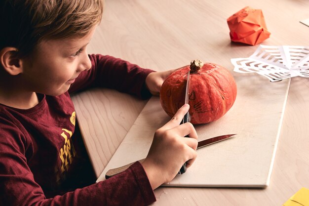 Halloween-, Dekorations- und Urlaubsideen - Nahaufnahme eines Kindes mit Messerschnitzerei Kürbis oder Jack-o-Laterne. Der 6-jährige Junge hat eine lustige Aktivität für die Familie. Mama verbringt Zeit mit Sohn zusammen