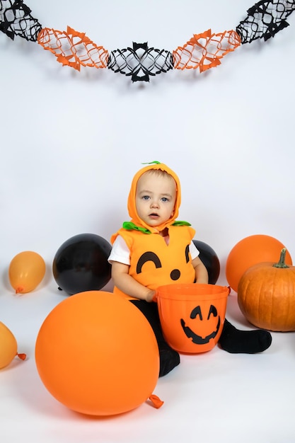 Halloween. Ein kleiner Junge in einem Kürbiskostüm sitzt mit einem Eimer, Luftballons herum