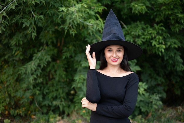 Halloween Eine junge schöne Frau in einem Hexenhut und einem schwarzen Kleid im Park Platz für Text