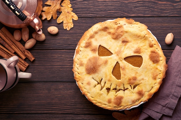 Halloween-Essen. Hausgemachter Kürbiskuchen oder Torte mit einem gruseligen Gesicht für Halloween auf einem Holztisch. Platz kopieren. Halloween-Food-Konzept.
