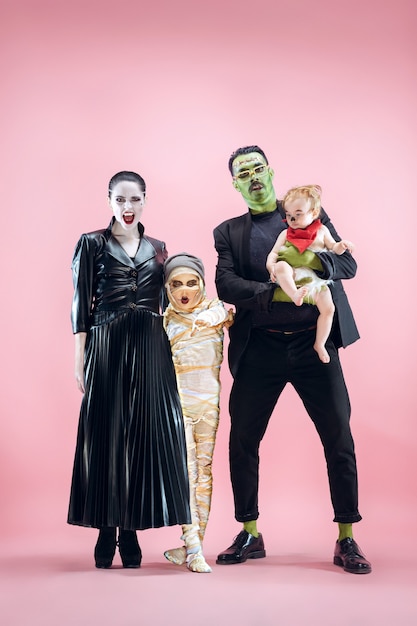 Halloween-Familie. Glücklicher Vater, Mutter und Kindermädchen in Halloween-Kostüm und Make-up. Blutiges Thema: die verrückten Maniak-Gesichter auf rosa Studiohintergrund