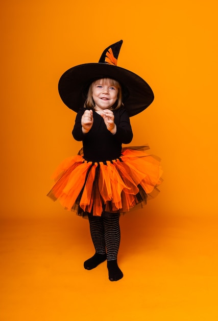 Halloween feiern. Kleines Mädchen, das als Hexe verkleidet ist, hält einen Eimer Kürbisse auf gelbem Hintergrund.
