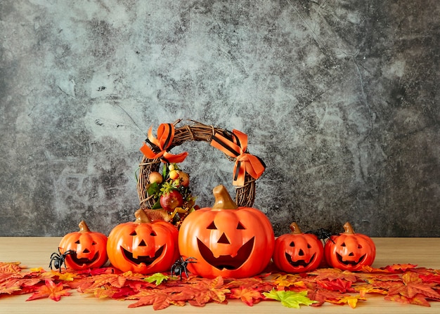 Halloween-Feiertagsdekoration mit Kürbiskopf-Klinkenlaterne und Herbstlaub auf Tischholz mit Betonwandhintergrund, Halloween-Hintergrundkonzept, Kopienraum.